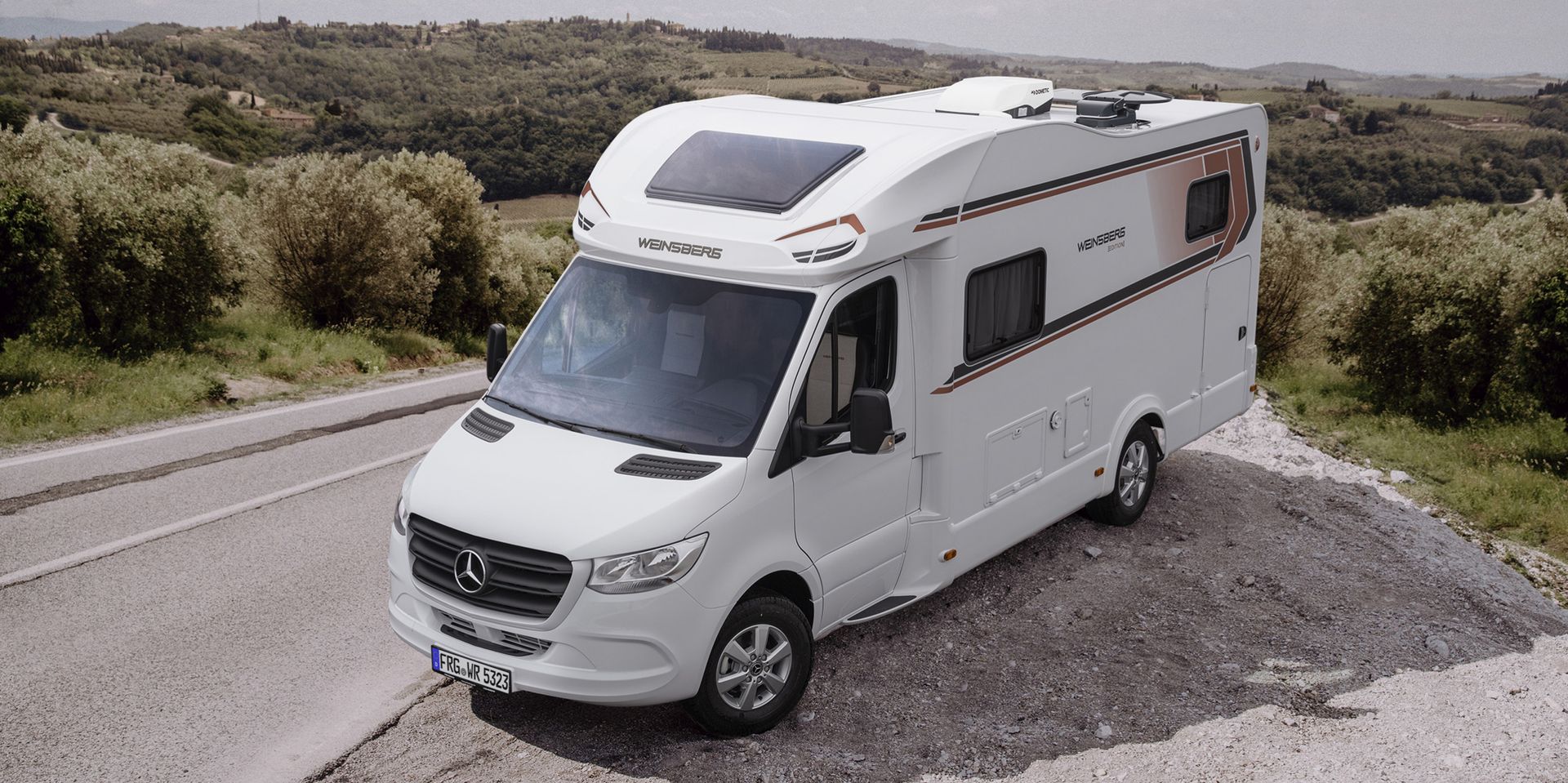 White camper van parked on gravel road with green landscape in the background.