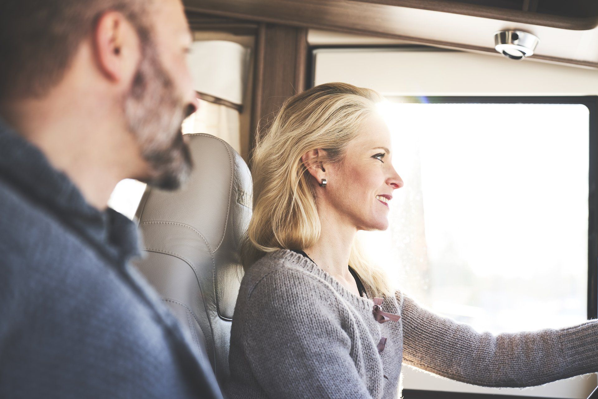 Woman driving RV, smiling, with man in passenger seat. Bright sunlight through window.