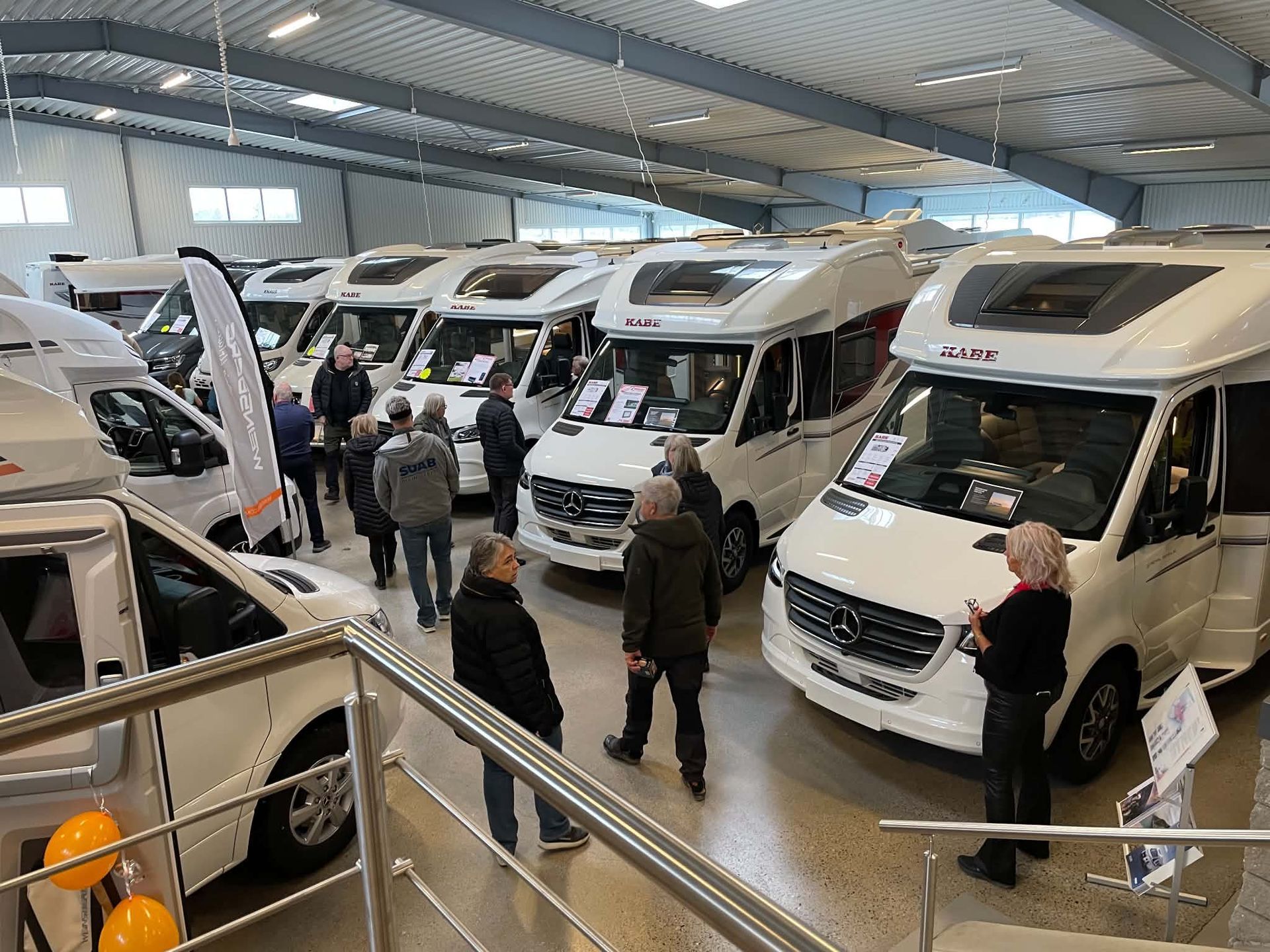 Indoor RV showroom with several white motorhomes and a few people browsing.