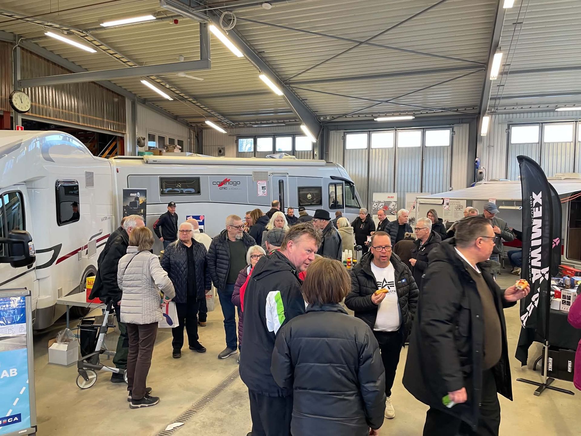 Crowded indoor RV show with people browsing camper vans under a large metal roof