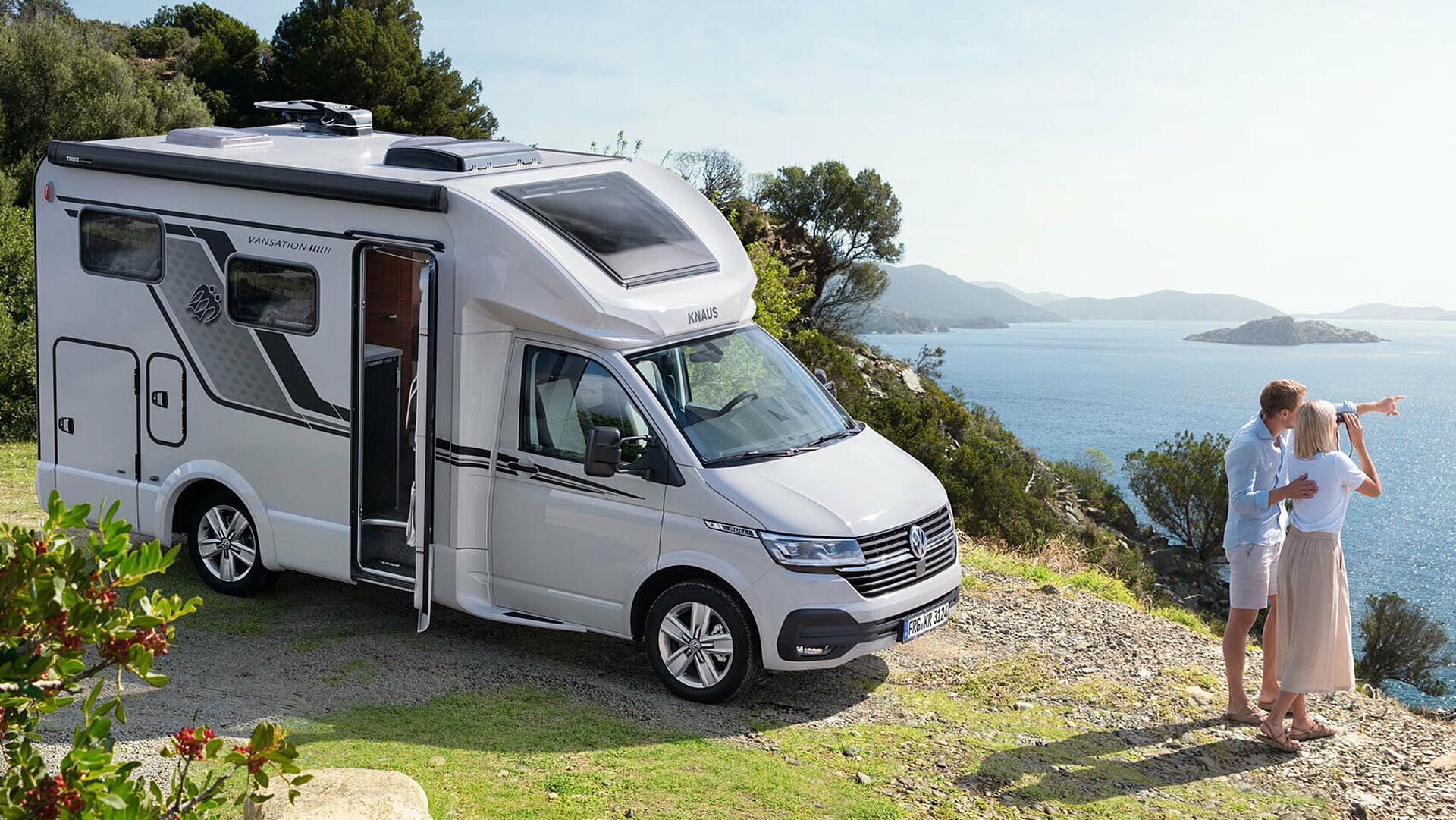 White RV parked on a hill overlooking the ocean, couple looking at the view.