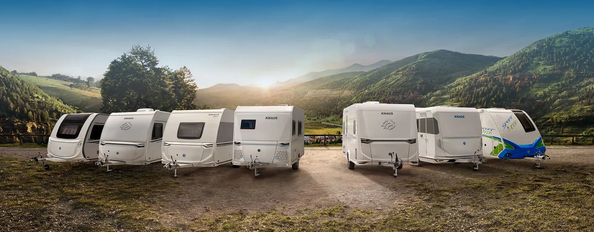 Several white RV trailers parked on a dirt road, mountains in the background.