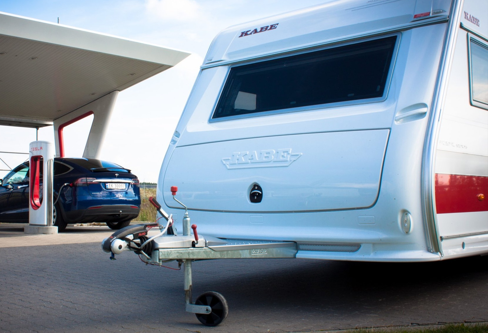 Blue Tesla charging at a station, towing a white travel trailer.