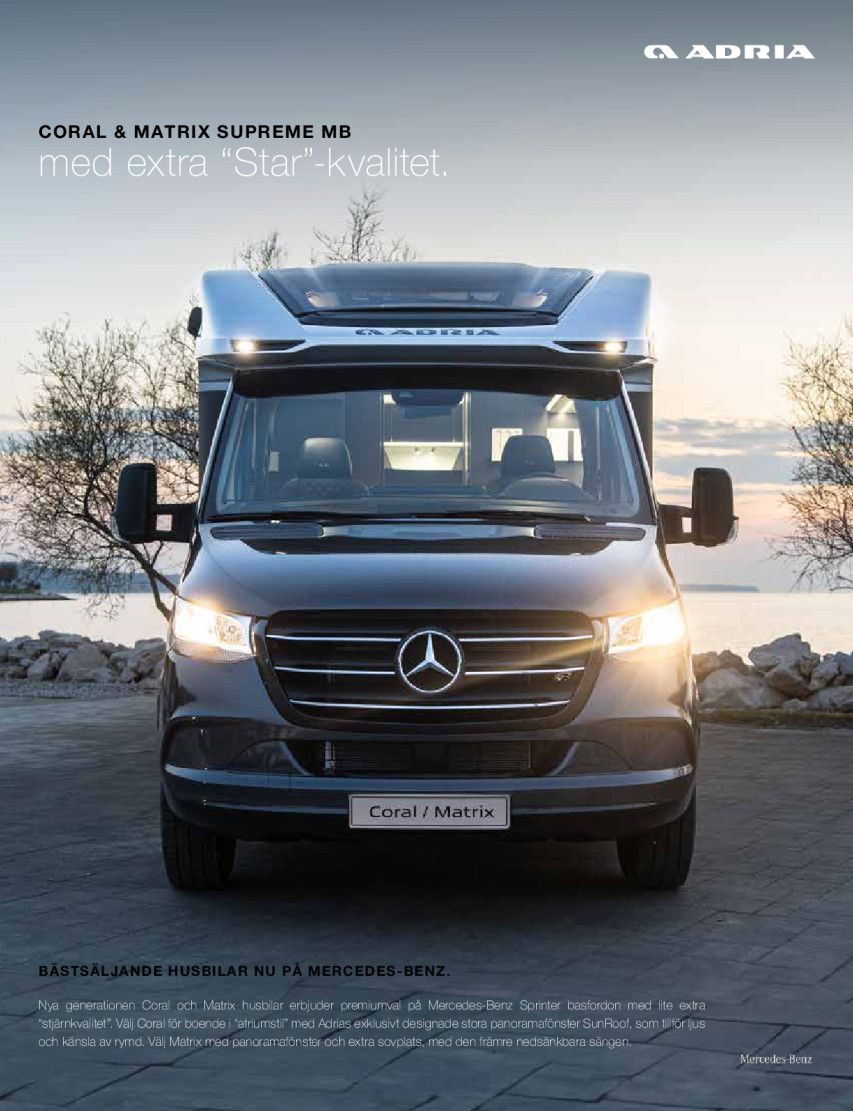 Dark gray Adria motorhome with bright lights, parked near water.