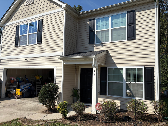 Two-story beige house with open garage, black shutters, and a front entry with a small porch