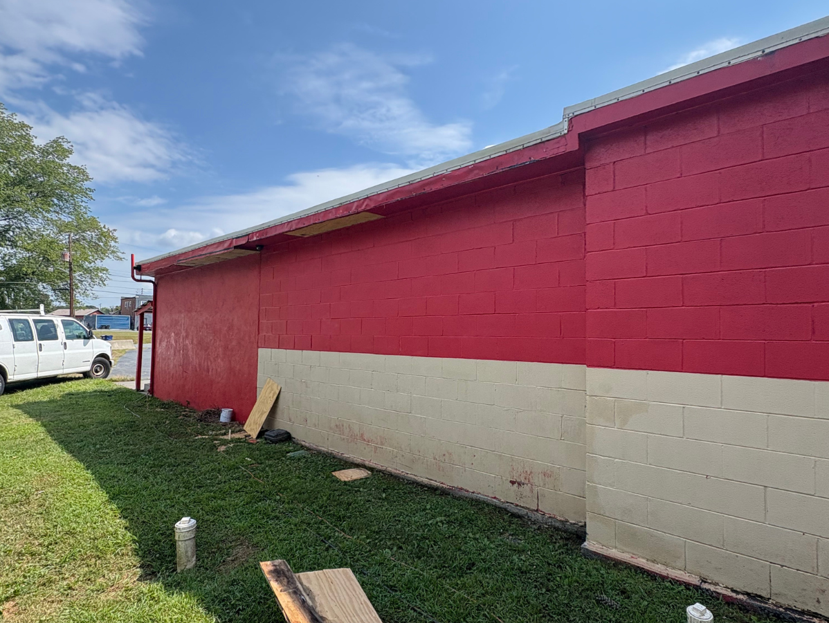 Red and white cinder block building beside a grassy lot under a blue sky