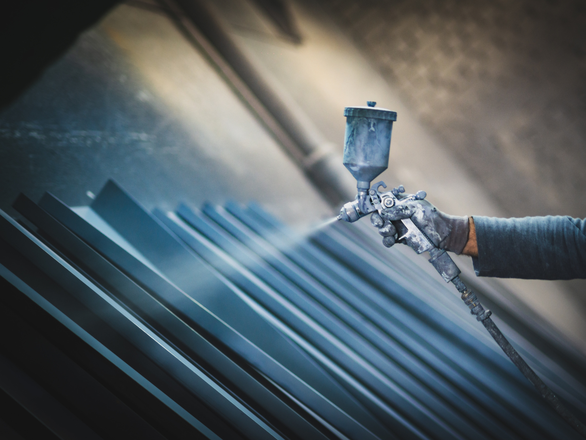 Spray gun coating blue metal panels in an industrial workshop