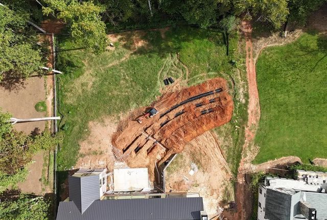 Aerial view of a curved rust-colored structure in a grassy lot beside buildings and trees.