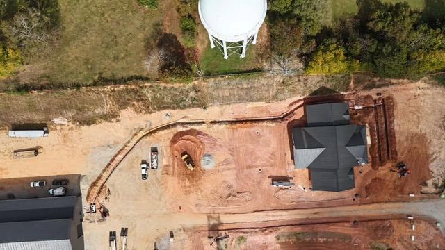 Aerial view of a construction site with a black-roofed house, dirt roads, and a white water tank nearby