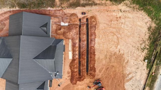 Aerial view of a house roof next to a long narrow trench in a dirt yard.