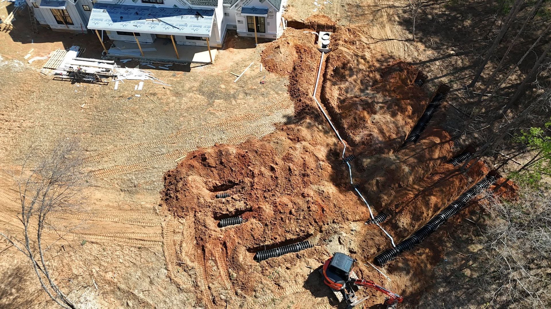 Aerial view of a muddy excavation pit beside a building, with a truck and equipment at the top edge.
