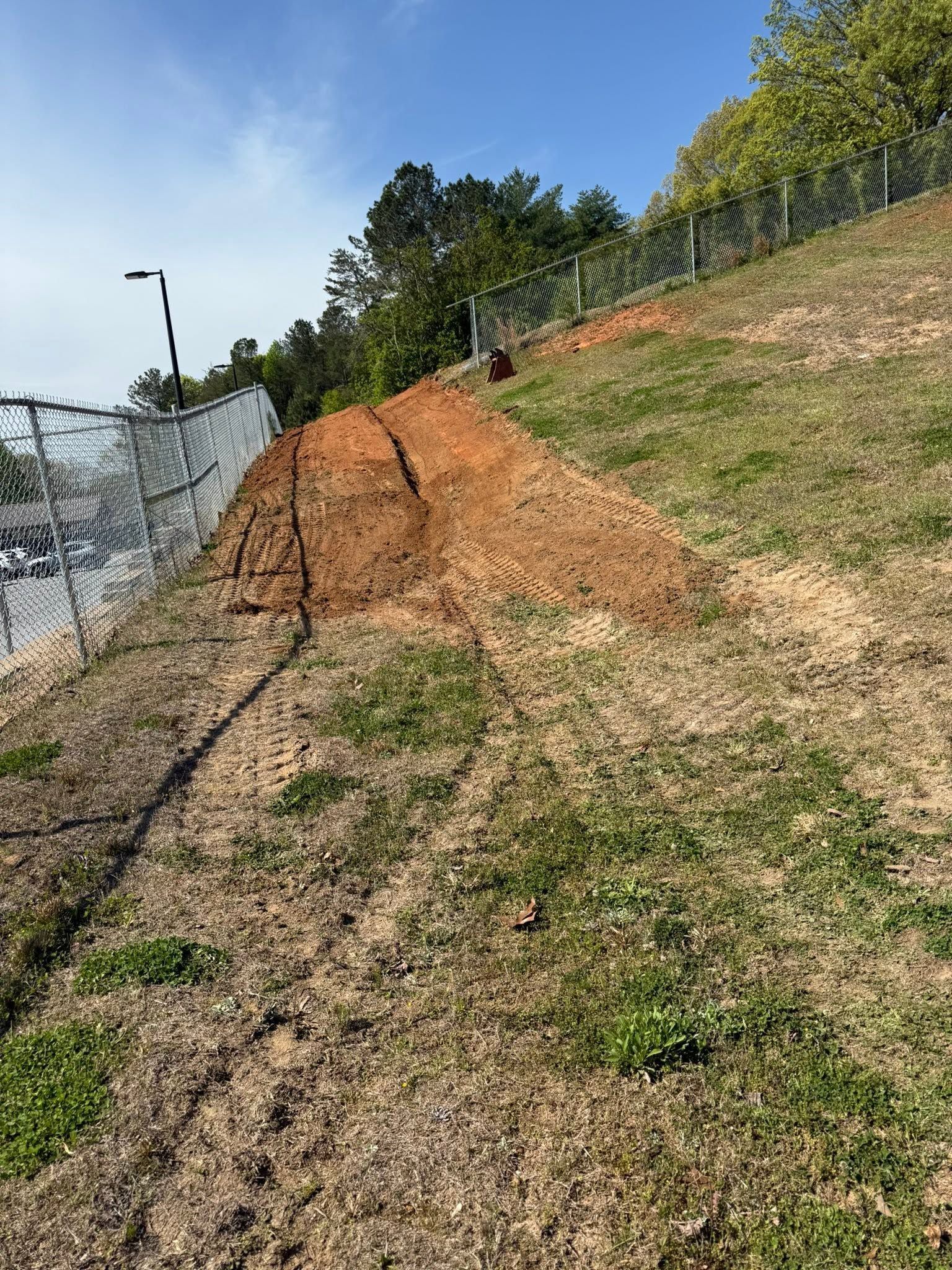 Eroded dirt slope beside a chain-link fence and grassy path under a clear blue sky