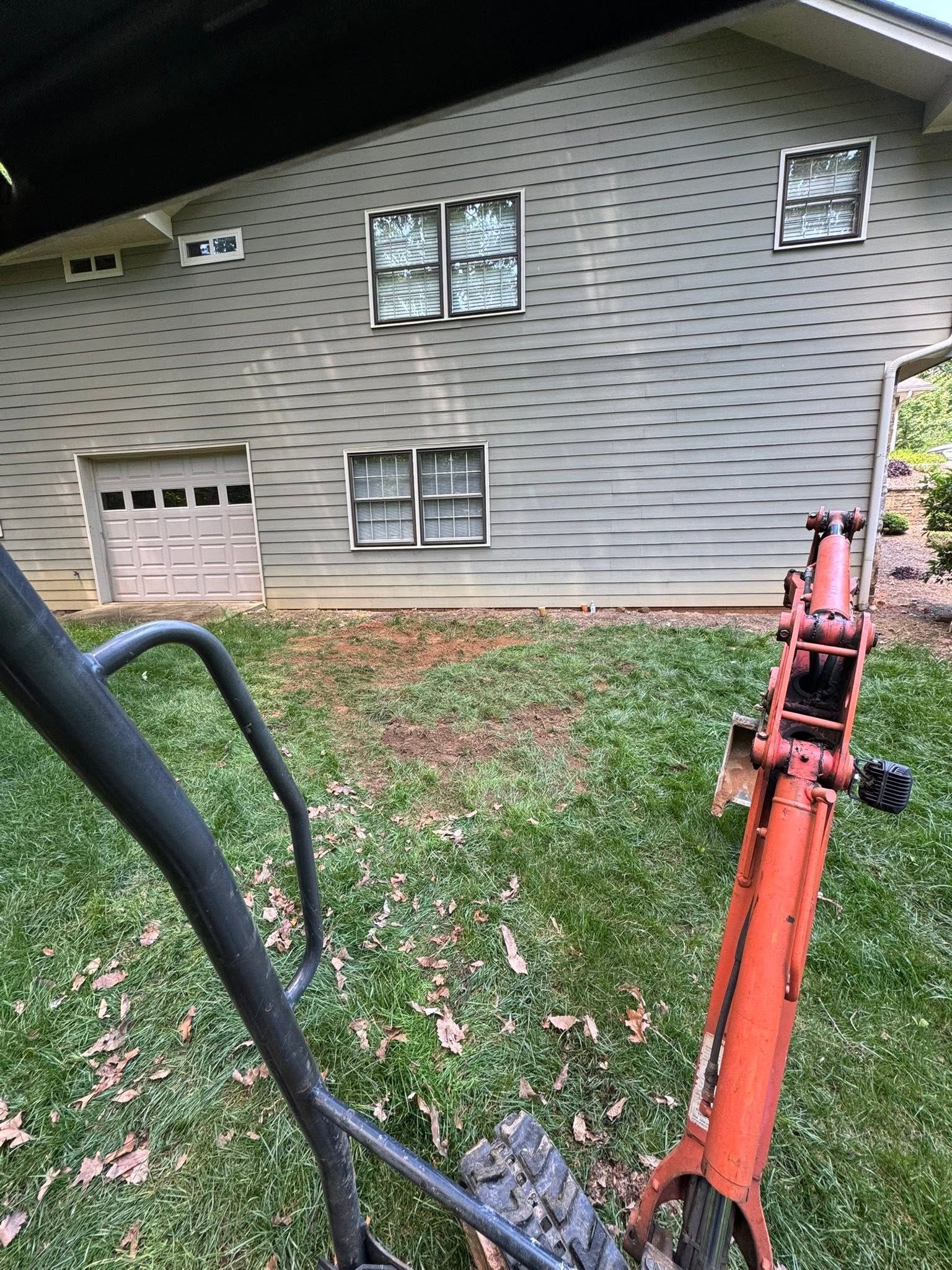 Side of a gray house with garage window, seen from a red ladder and black railing in the foreground.