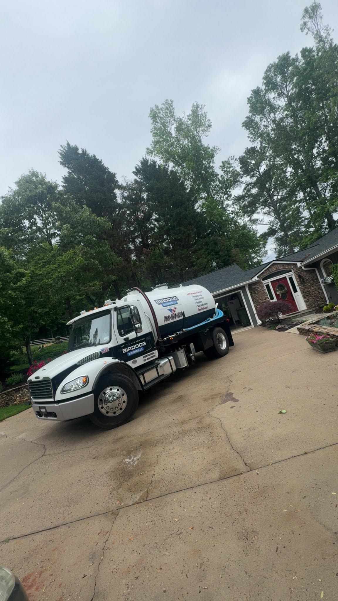 White utility truck parked on a wet driveway beside a house and trees.