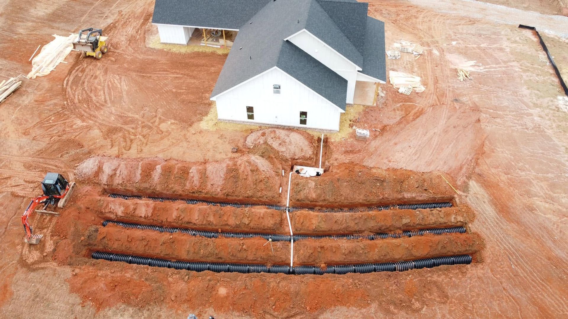 Aerial view of a white house under construction with excavators and trenches on a dirt lot