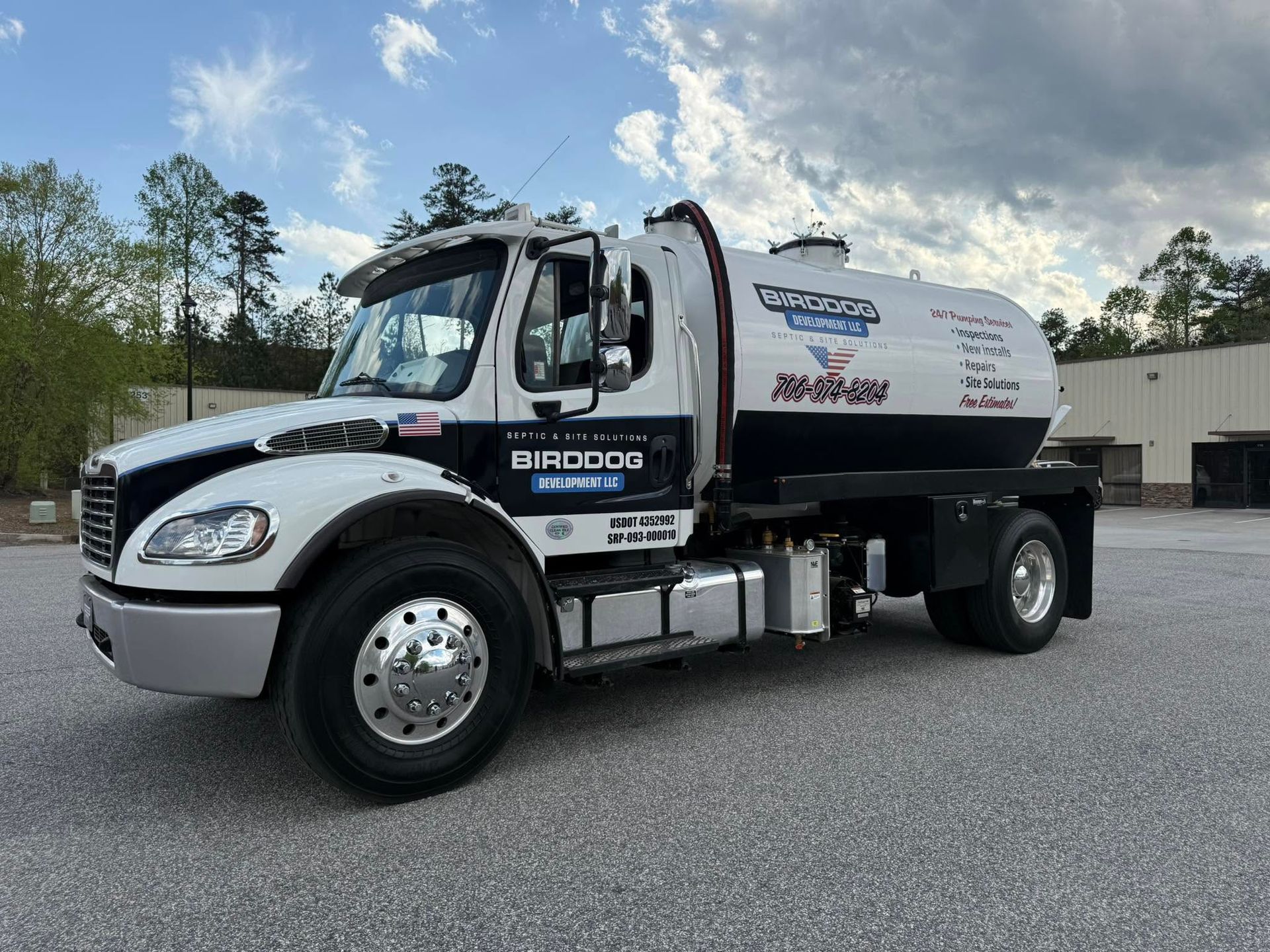 White and black tanker truck parked on gravel lot under a cloudy sky