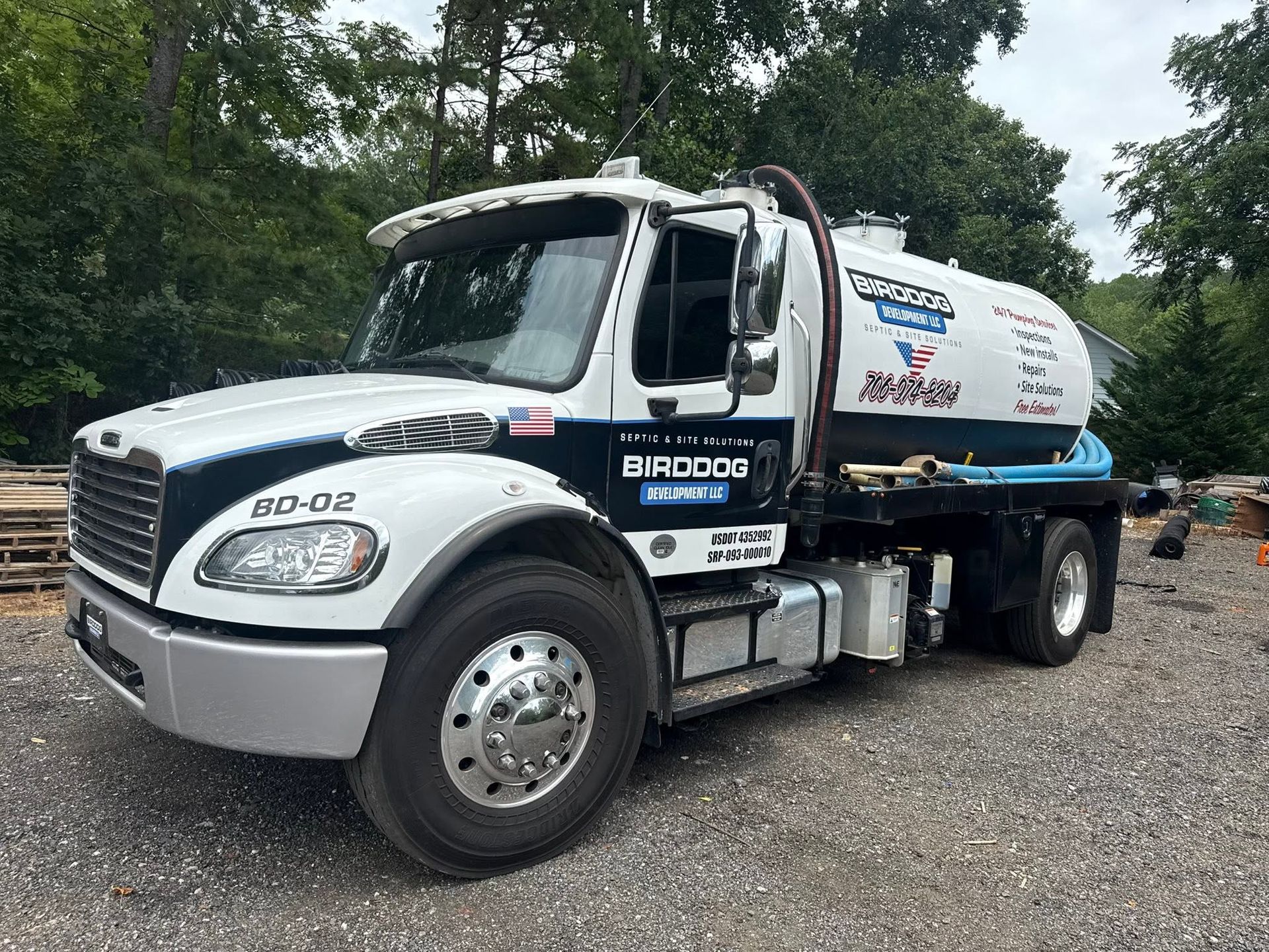 White tanker truck parked on gravel with trees in the background