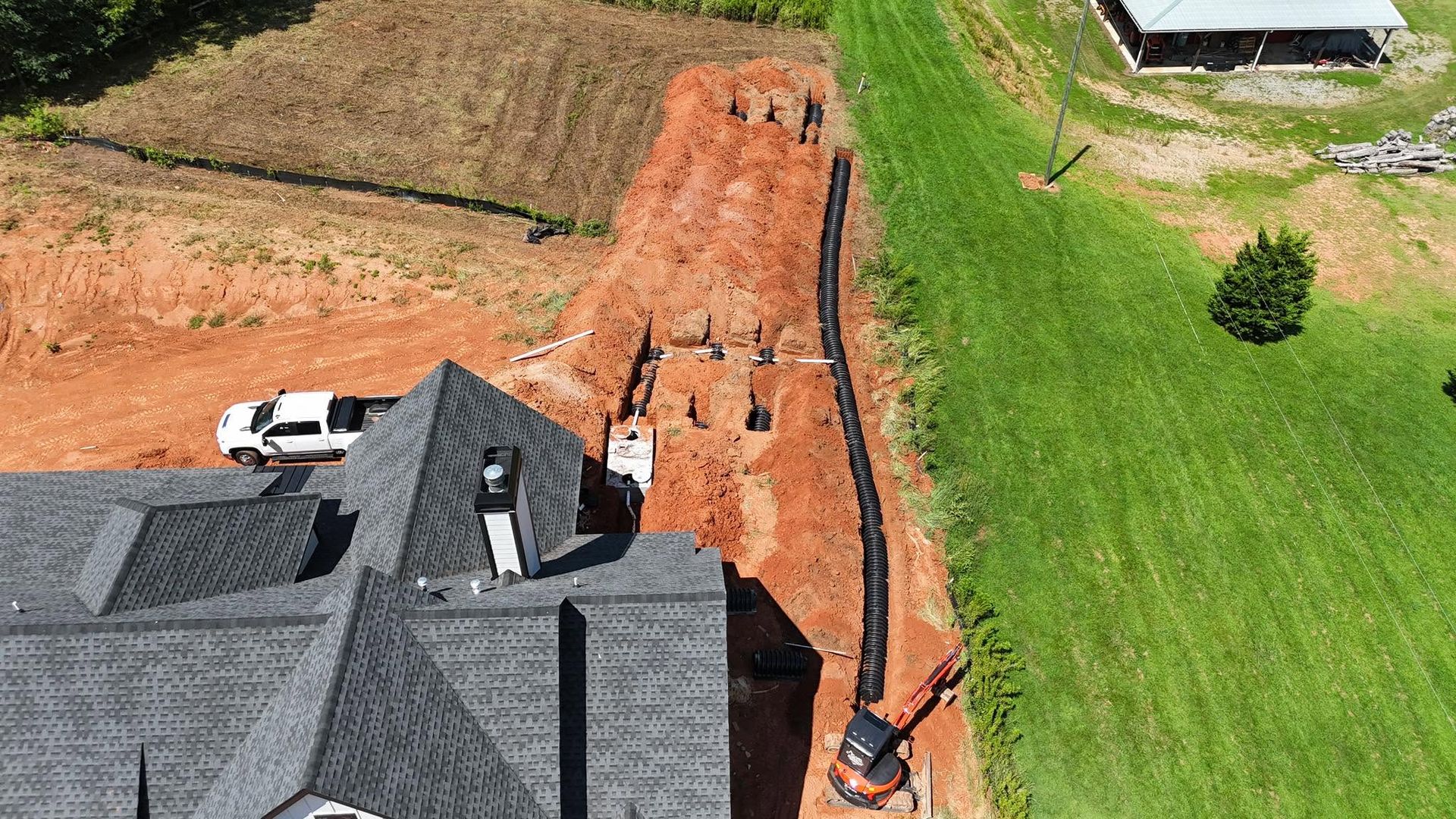 Aerial view of a house beside a long orange dirt trench cutting through a green lawn