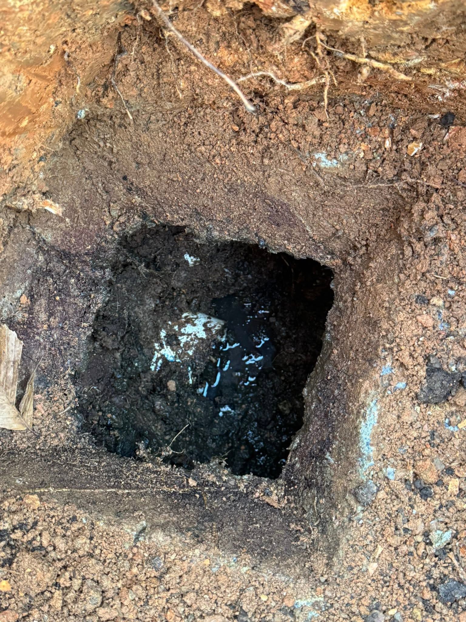Square hole in dirt exposing dark water or mud inside an excavation site.