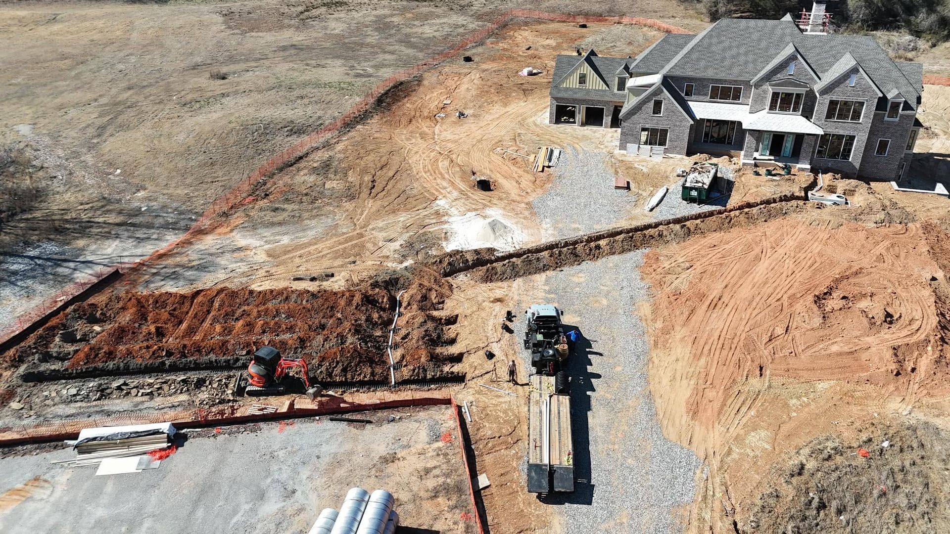 Aerial view of a house under construction with excavators, dirt piles, and a concrete foundation site.