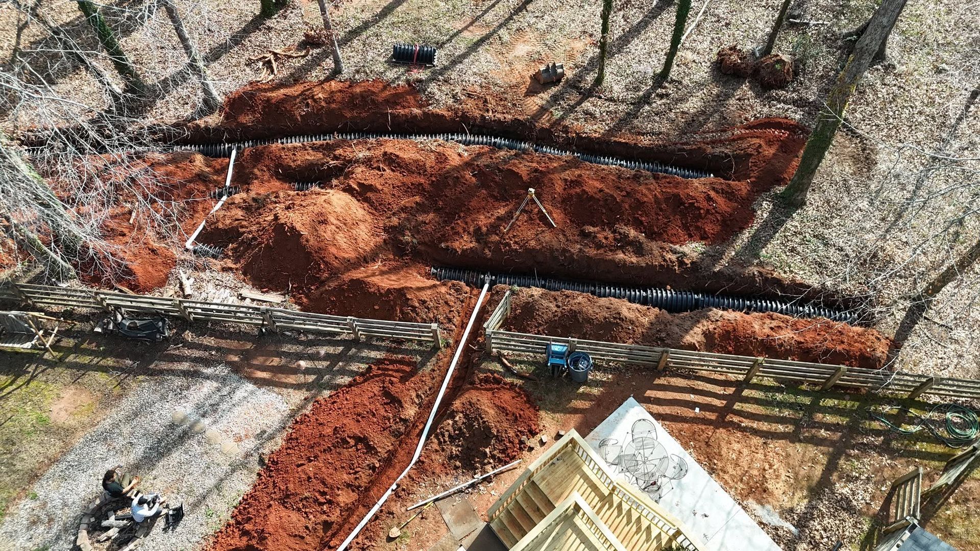 Aerial view of a large rust-colored excavation pit beside a road and fence.