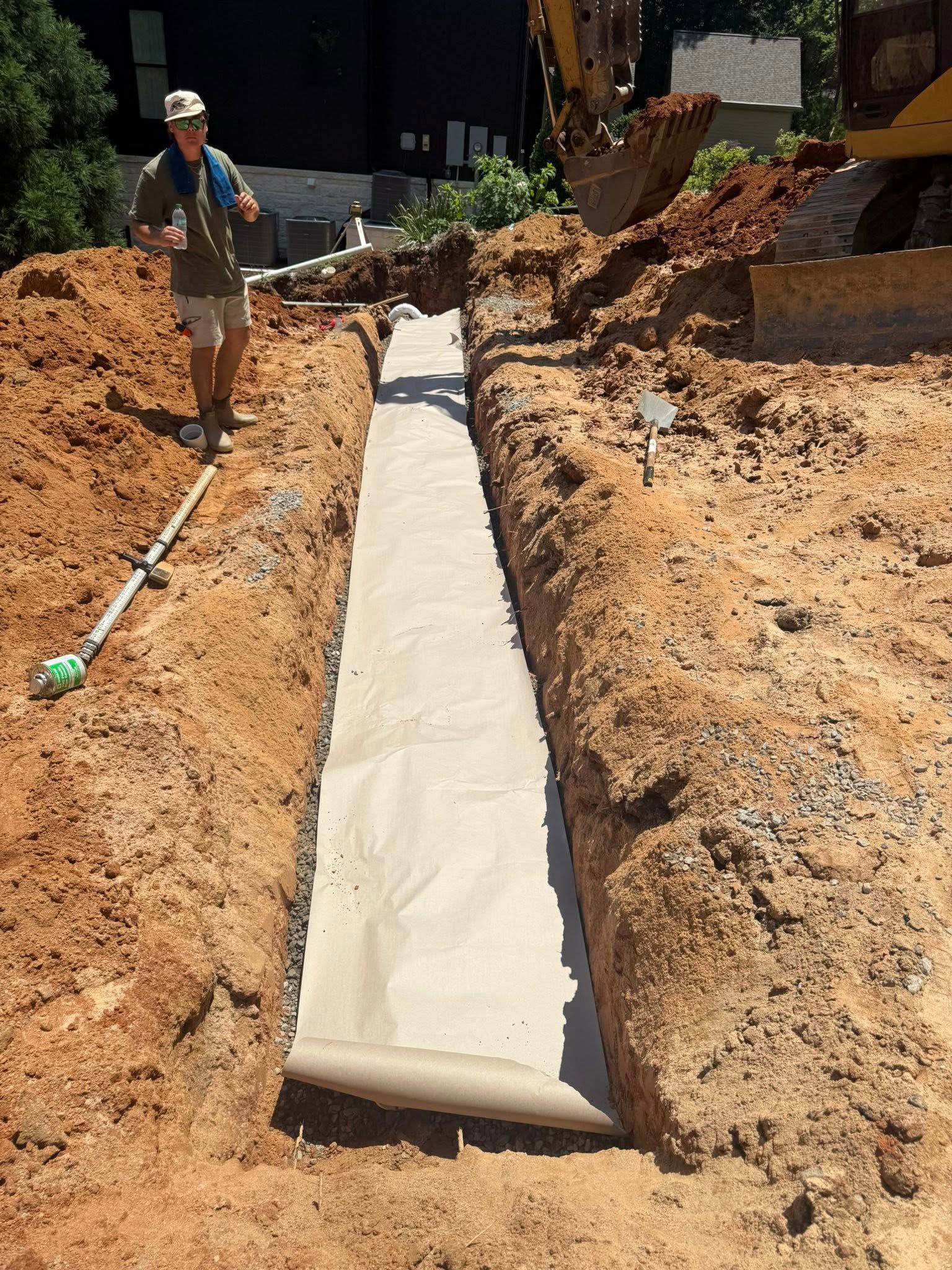 Person standing beside a long concrete trench in a dirt excavation site.