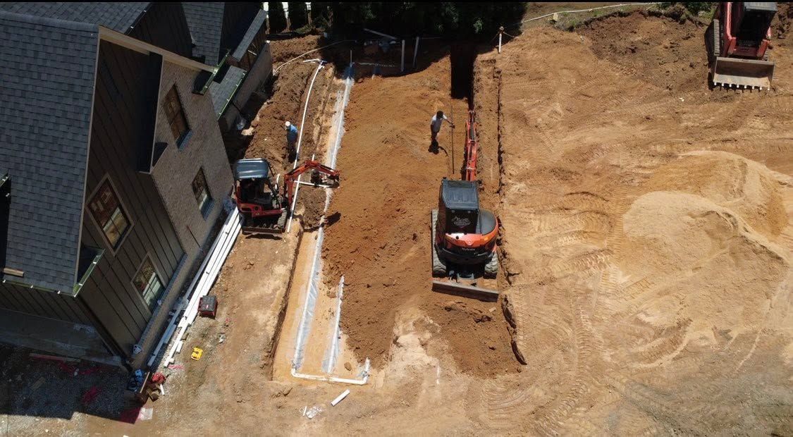 Aerial view of a house construction site with a bobcat, workers, and dirt grading around a new foundation.