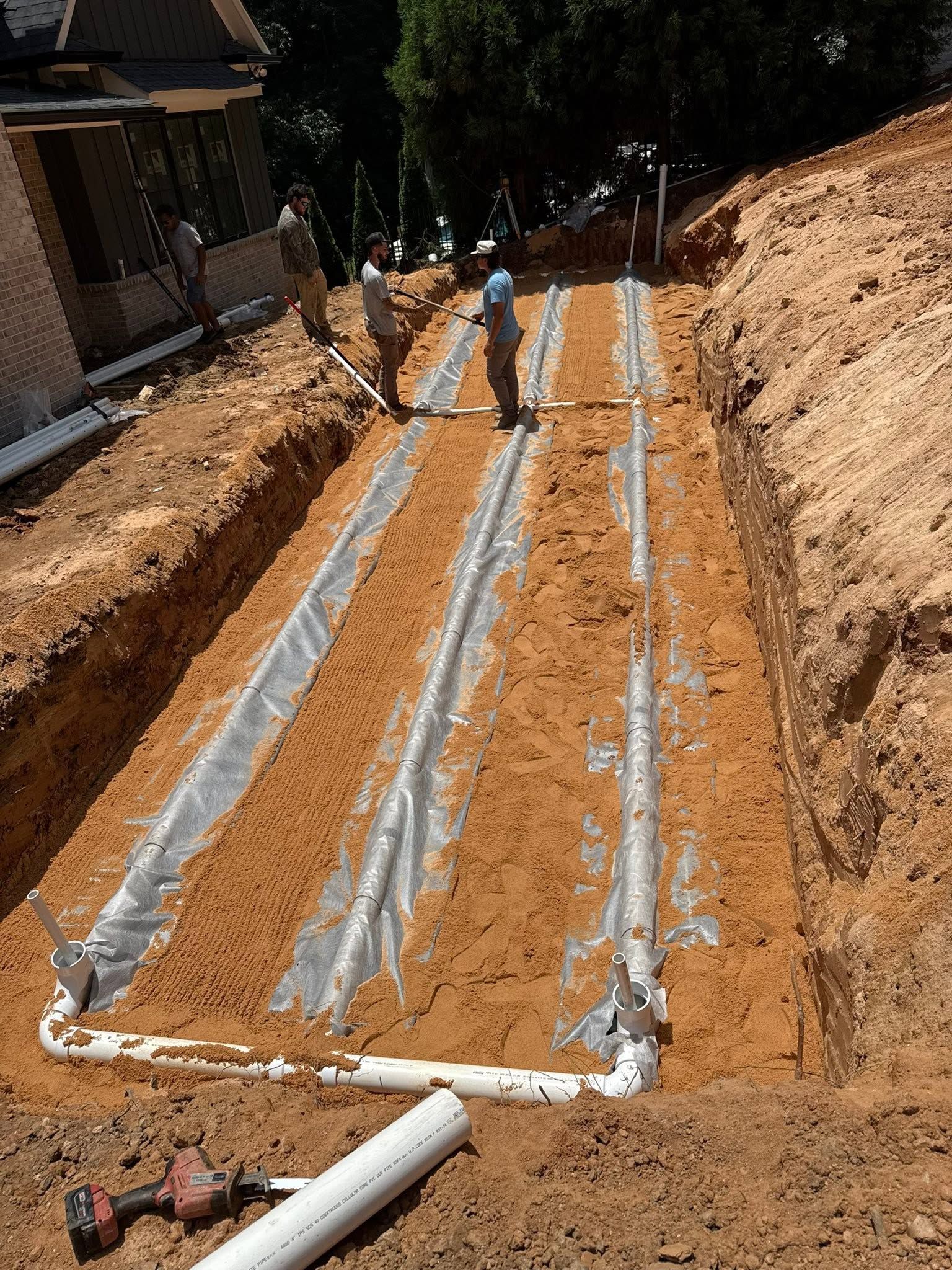 Excavation site with long white-lined trenches in reddish soil and two workers standing at the far end