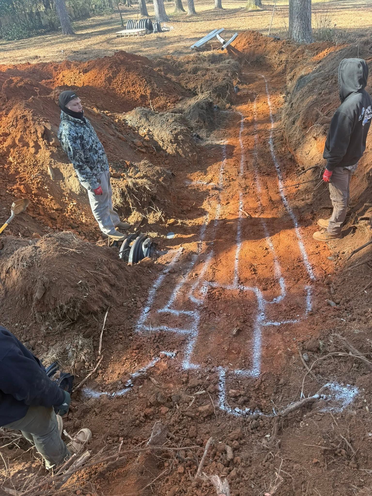 People marking a dug-out excavation with white chalk lines on dirt outdoors