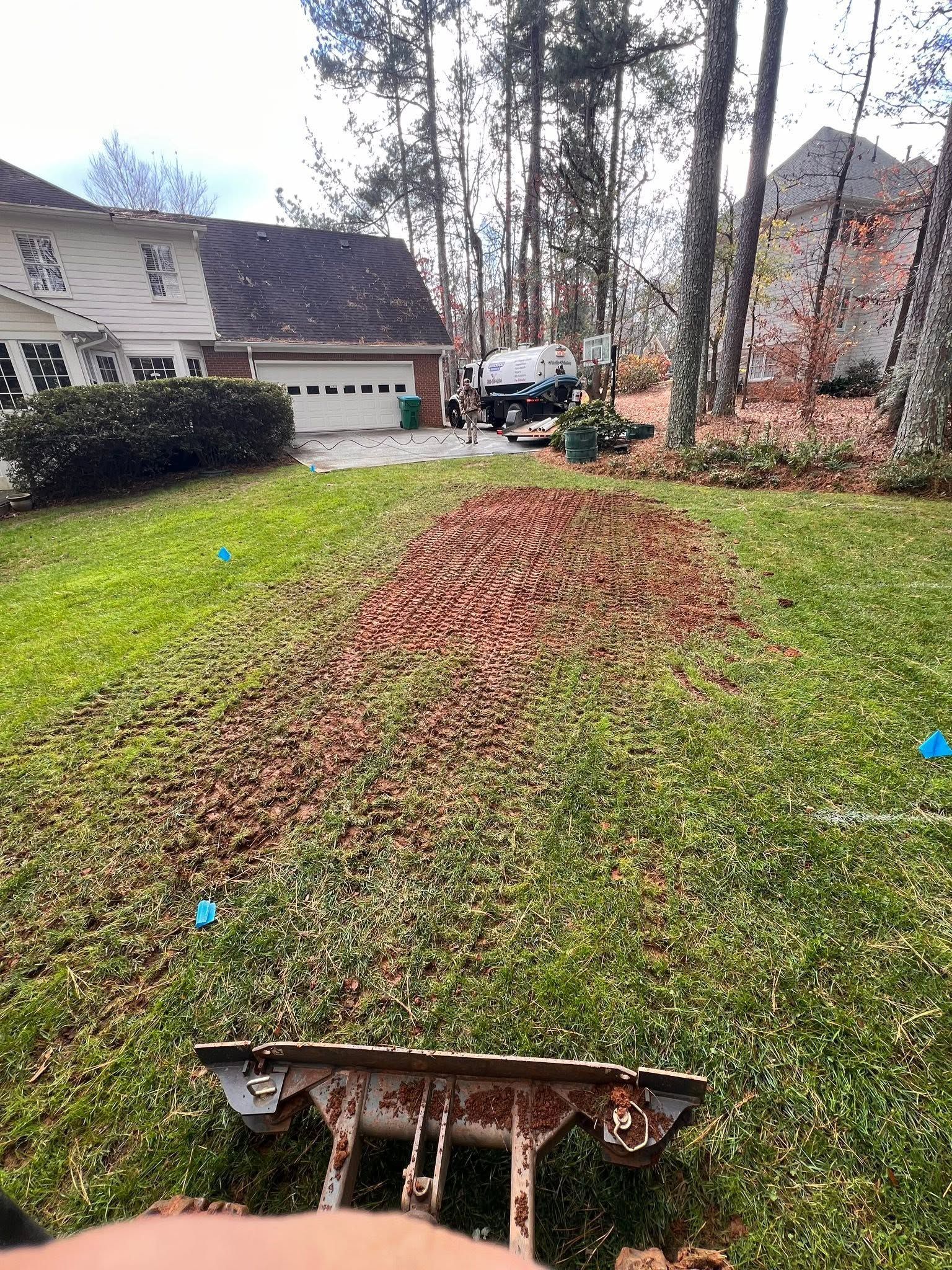 Leaf-covered front yard with a small dirt mound, trees, and houses in the background