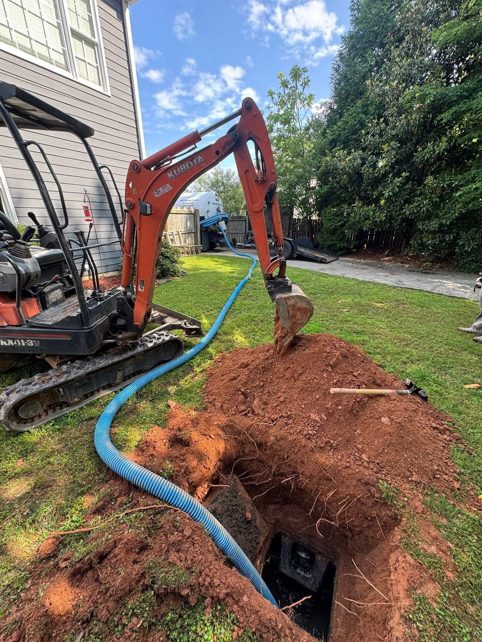 Mini excavator digging a trench by a house, with a blue hose and dirt pile on a lawn.