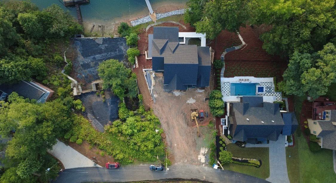 Aerial view of three houses surrounded by trees along a curved road, with a pool visible on the right.