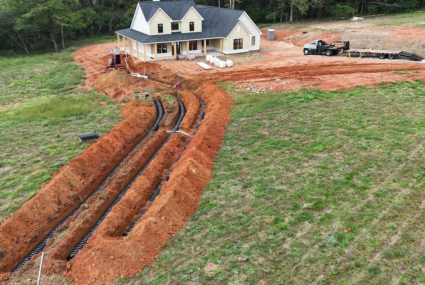 New house under construction with muddy driveway cuts and a parked truck on a grassy lot