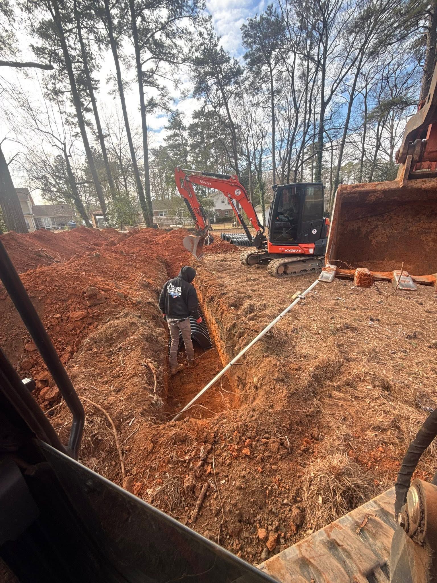 Excavator and worker in a leaf-filled woodland clearing, with a rope stretched across the ground.
