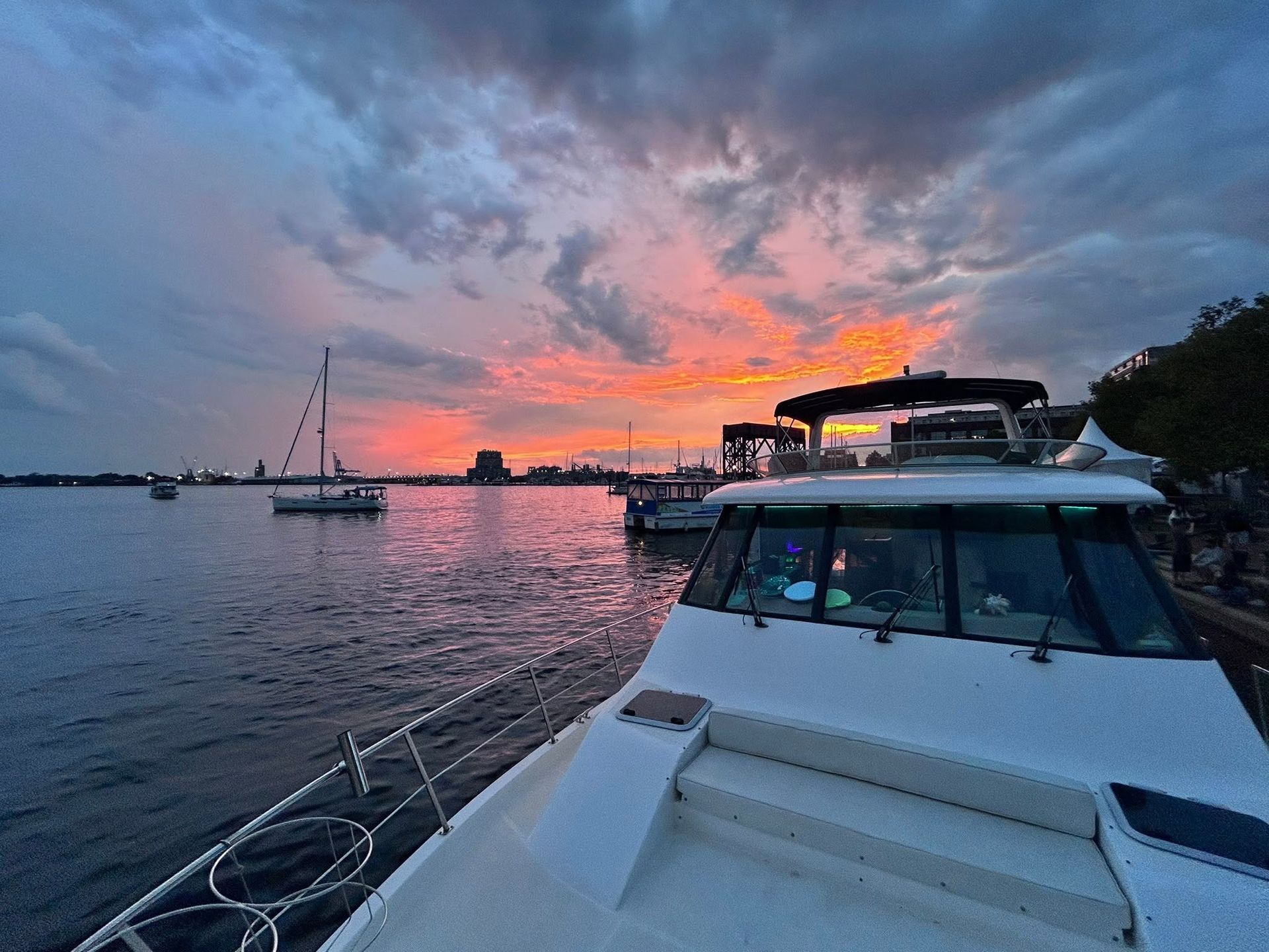 Sunset over calm water with boats docked at a marina and a pink-orange sky