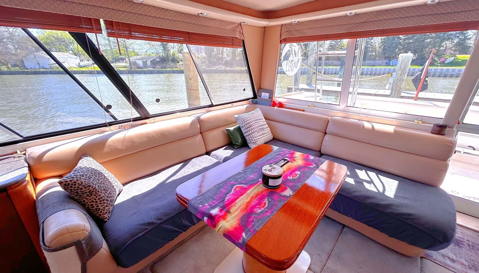 Covered outdoor lounge with tan sectional, colorful table, and bright sunlight through screened windows