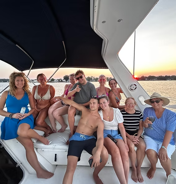Group of people relaxing on a boat at sunset, smiling and sitting under a canopy.