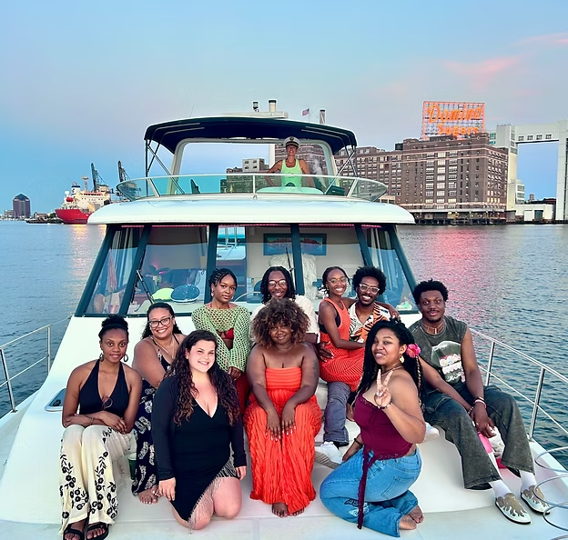 Group posing on a boat deck with city skyline in the background during sunset.