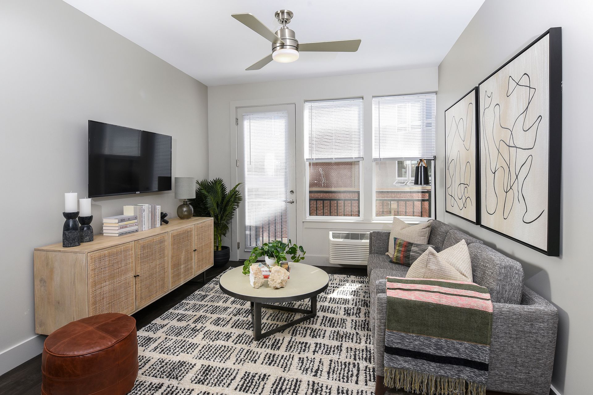 Living room with TV, sofa, coffee table, rug, and artwork. A balcony is visible through the window.