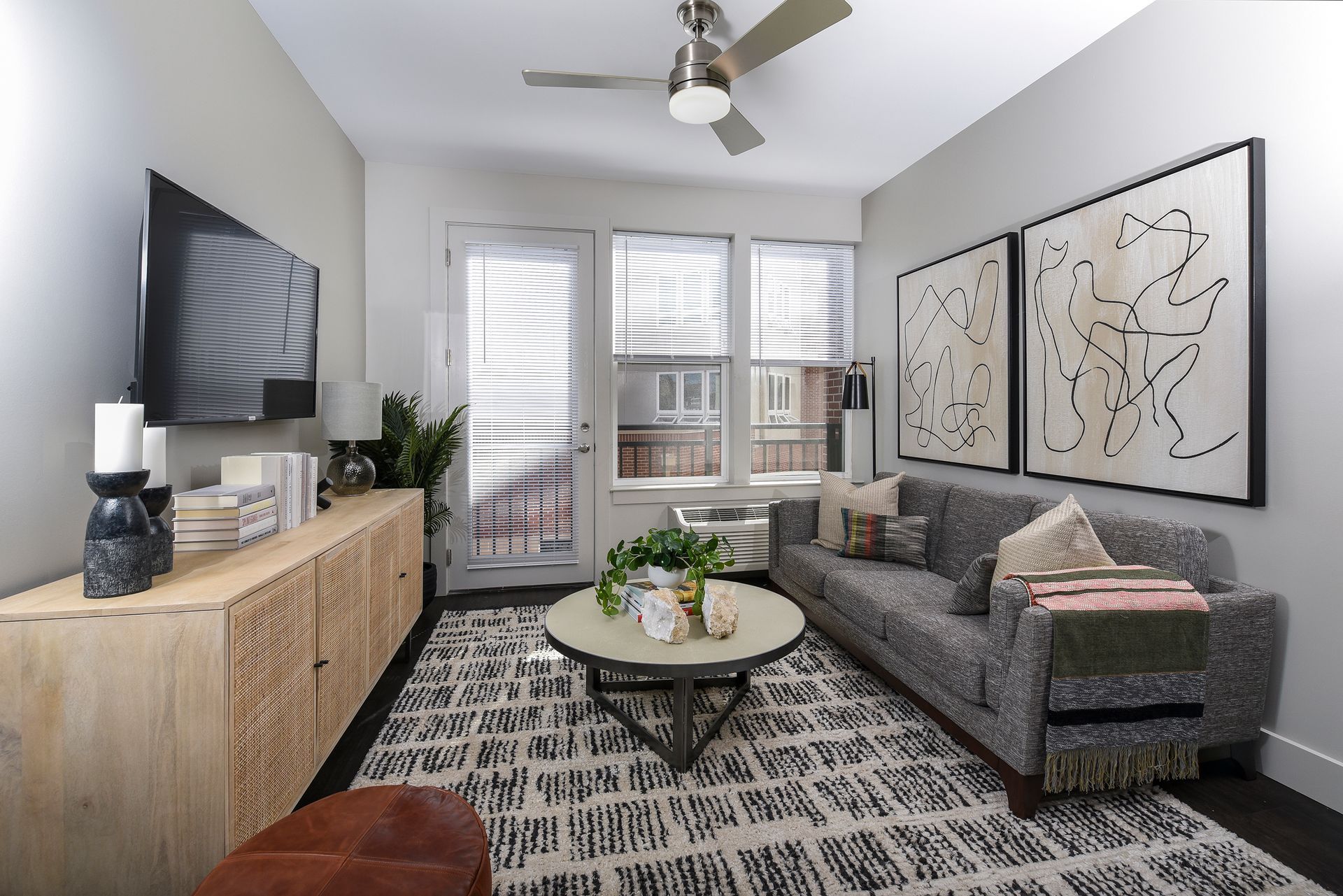Living room with a sofa, rug, coffee table, art, TV, and light wood entertainment unit.