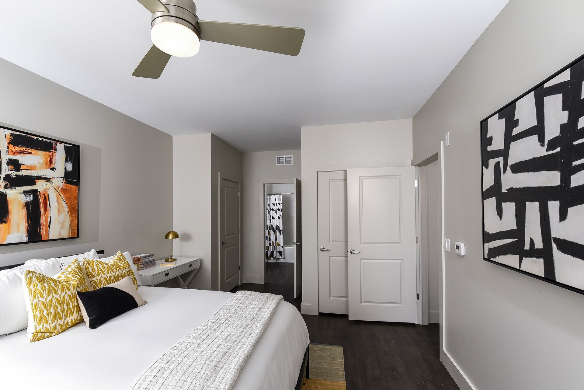 Bedroom with a bed, desk, art, and a closet. Neutral walls, dark floor, and a ceiling fan.