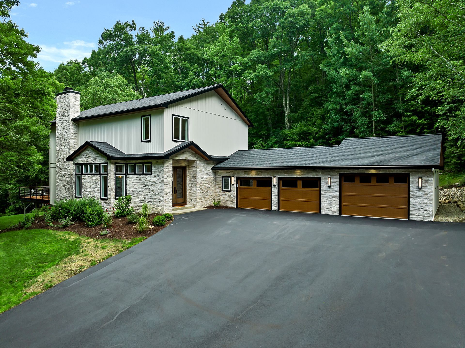 A house with three garage doors is surrounded by trees