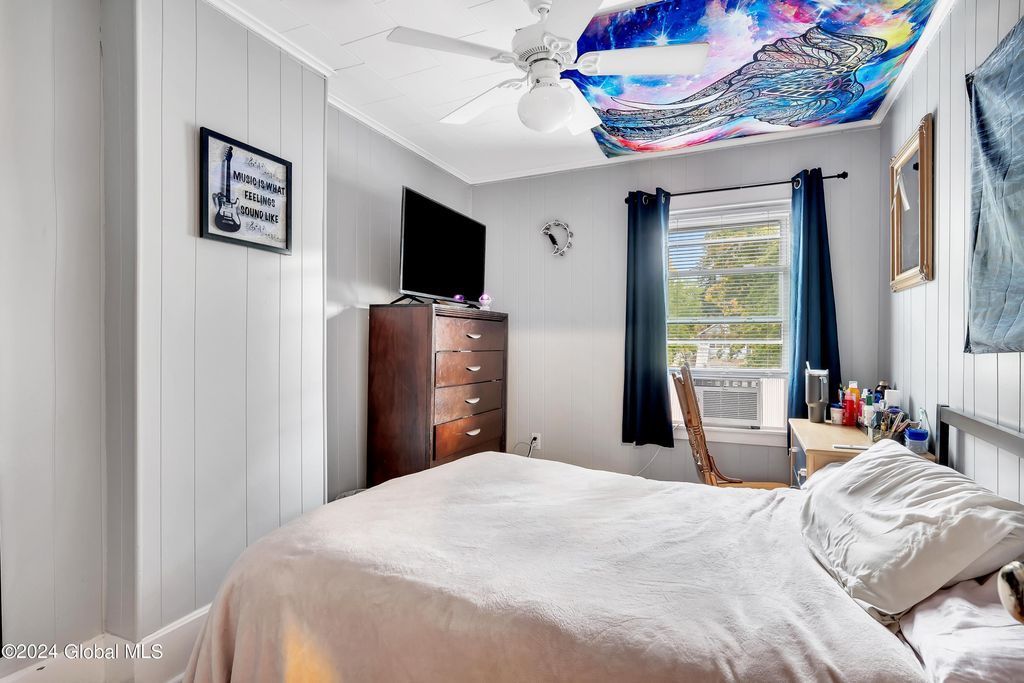 A bedroom with a bed , dresser , television and ceiling fan.