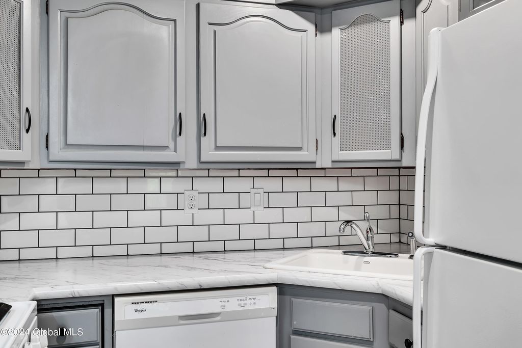 A kitchen with white cabinets , a refrigerator , a dishwasher , and a sink.