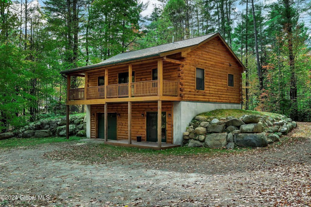 A large log cabin with a porch in the middle of a forest.