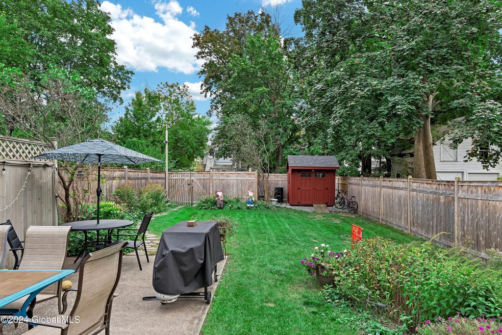 A backyard with a table , chairs , umbrellas and a shed.