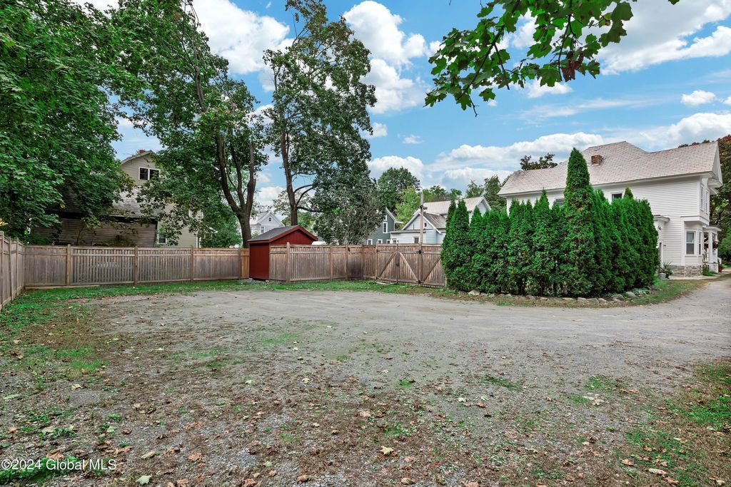 A gravel driveway leading to a house with a fence and trees in the background.