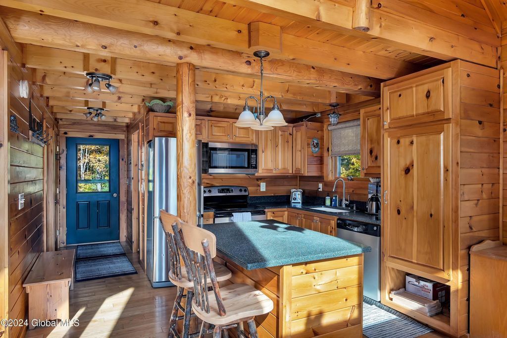 A kitchen in a log cabin with wooden cabinets and stainless steel appliances.
