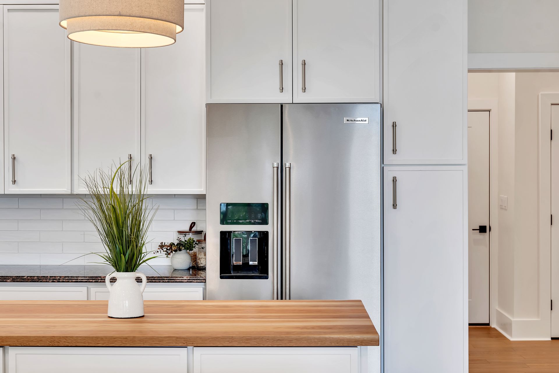 A kitchen with white cabinets , a stainless steel refrigerator and a wooden counter top.