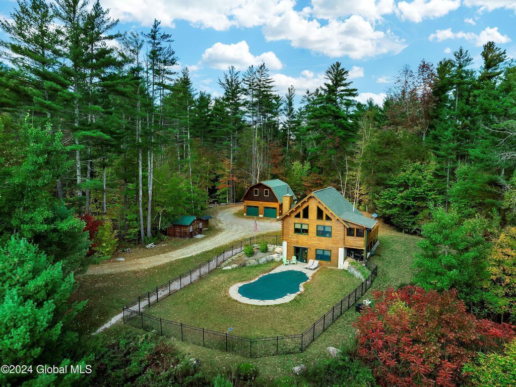 An aerial view of a log cabin with a pool in the middle of a forest.